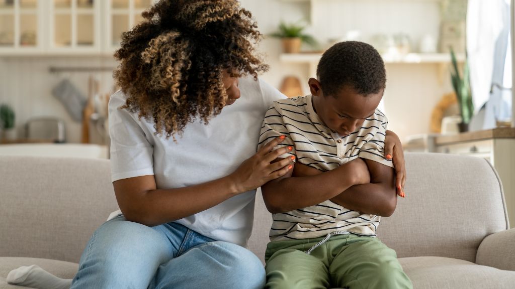 A parent sitting beside a child on a sofa, offering calm support during an emotional moment, illustrating how to talk to kids about mental health.