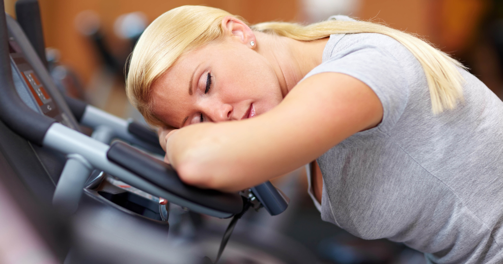 A woman resting her head on gym equipment mid-workout, showing how exercise can become too comfortable and stall weight loss progress.